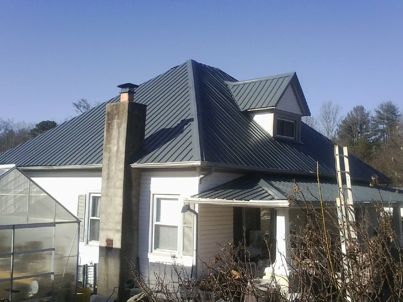 Dark blue standing seam metal roof on a white farmhouse with dormer — Slate & Tile Roof Repair by Roofing Brothers in Peachtree Corners