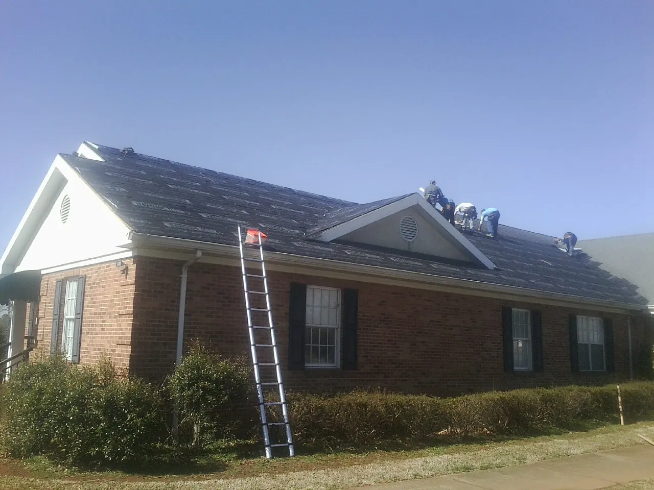 Crew tearing shingles off a brick ranch roof with a ladder set — Emergency Roof Repair work by our crew in Peachtree Corners