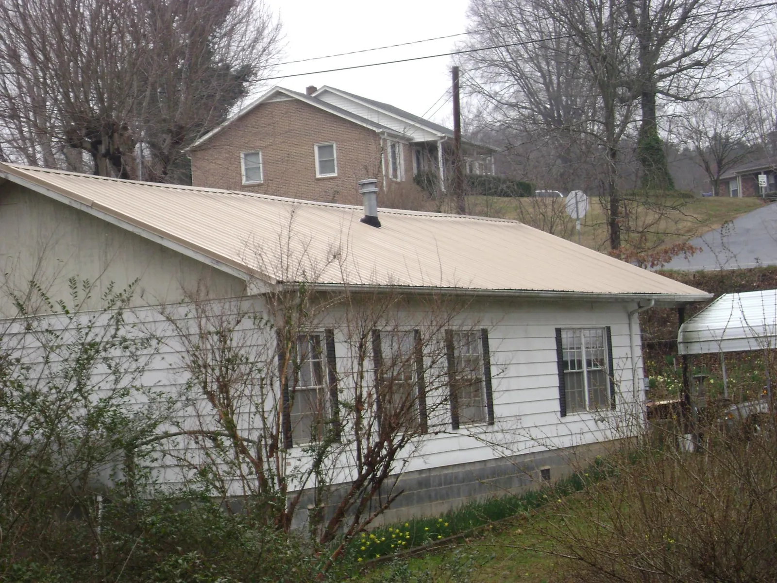 Tan metal roof on a white sided house set into a hillside — Commercial Roofing by Roofing Brothers in Peachtree Corners
